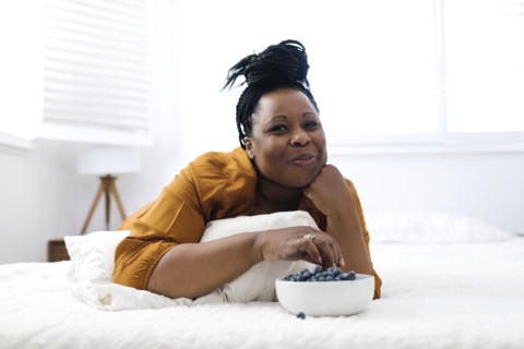 Woman lying on bed, eating blueberries and watching tv
