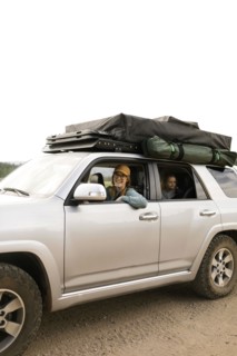Smiling woman with daughter (6-7) sitting in off road car with tent on roof