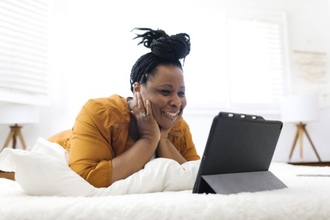 Smiling woman lying on bed and looking at tablet