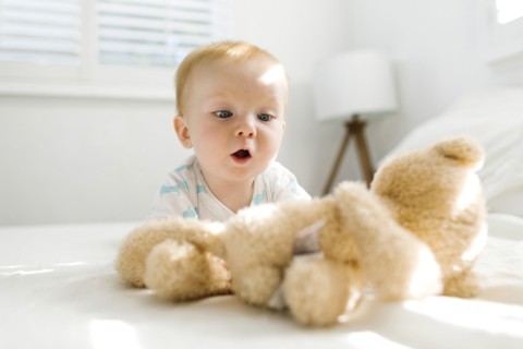 Baby boy (6-11 months) looking at teddy bear on bed