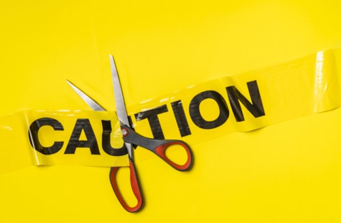 Studio shot of scissors cutting caution tape on yellow background