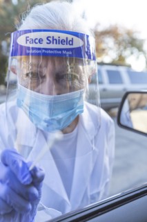Female medical staff in protective clothing approaching car with coronavirus swab test