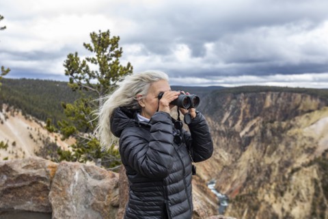 Senior woman looking through binoculars while standing above Grand Canyon in Yellowstone National Park
