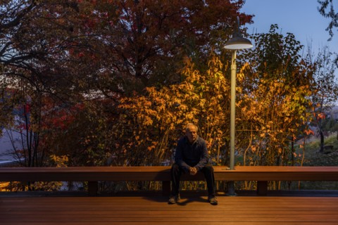 Senior man sitting on deck bench under autumn tree illuminated at night