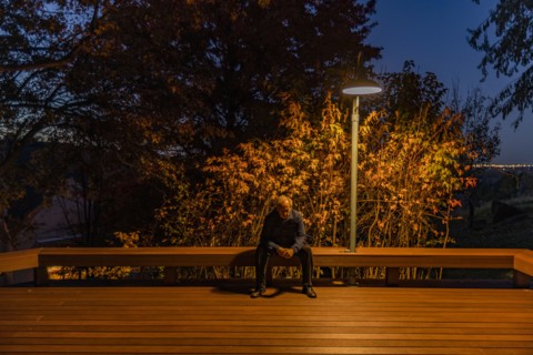Senior man sitting on deck bench under autumn tree illuminated at night