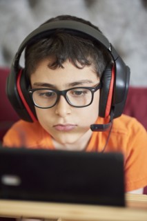 Boy (8-9) gaming on tablet while sitting in bed during weekend