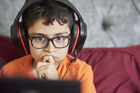 Boy (8-9) gaming on tablet while sitting in bed during weekend