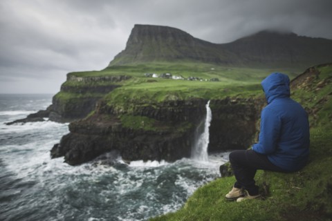 Man sitting on edge of cliff and looking at Mulafossur Waterfall