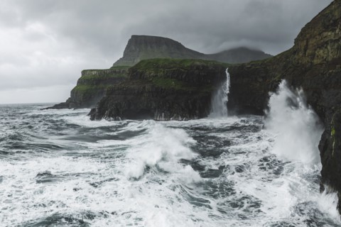 Coastline with Mulafossur Waterfall falling into Atlantic Ocean in stormy day