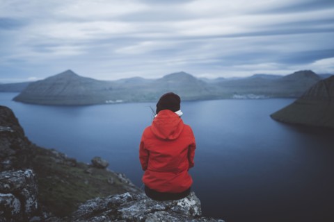 Woman sitting on edge of cliff over sea and looking at view