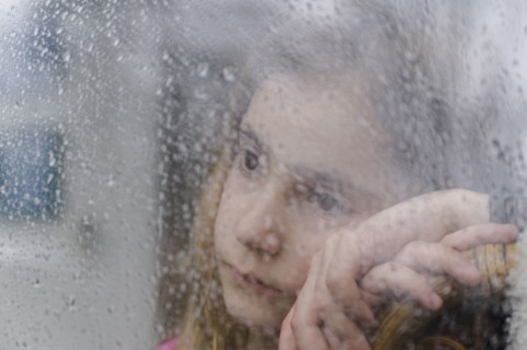 Close-up of girl (8-9) looking through window on rainy day