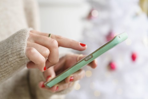 Hands holding smartphone next to Christmas tree
