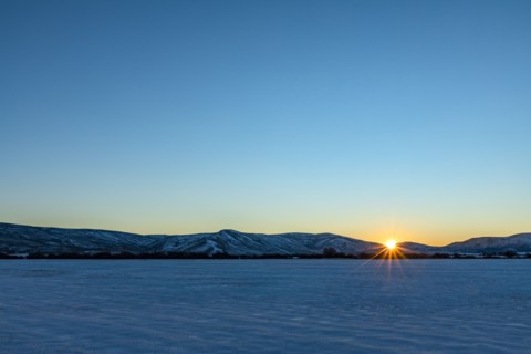 Sun setting over snowy field and mountains