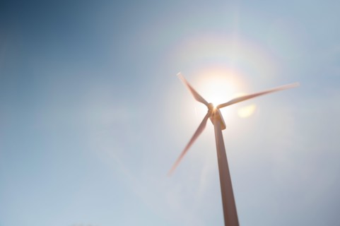 Low angle view of wind turbine against blue sky and sun