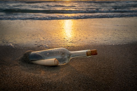 Glass bottle with message inside on beach at sunset