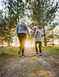 Rear view of mother and daughter holding hands and walking in landscape at sunset