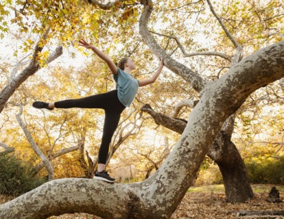 Girl standing on one leg on tree in forest at sunset