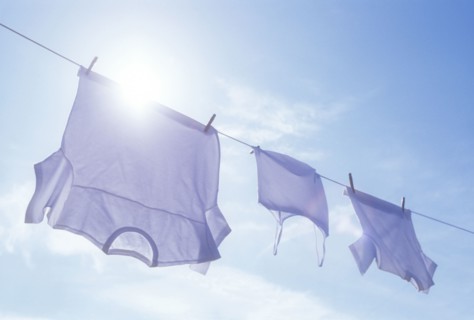 Low angle view of laundry drying on clothesline against sky and sun