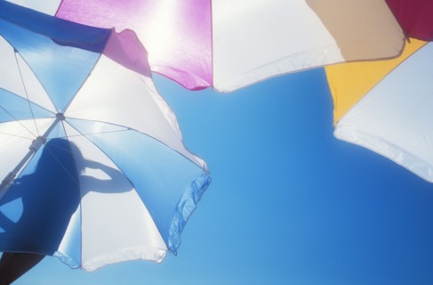 Low angle view of silhouette of woman on beach umbrella against blue sky