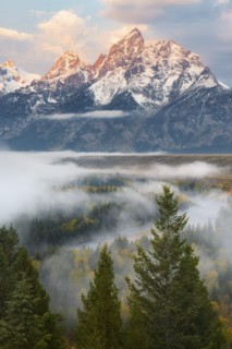 Snow covered Teton mountains at sunrise with mist above forest in foreground
