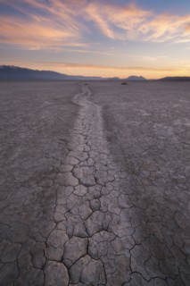 Path at cracked desert area at sunset