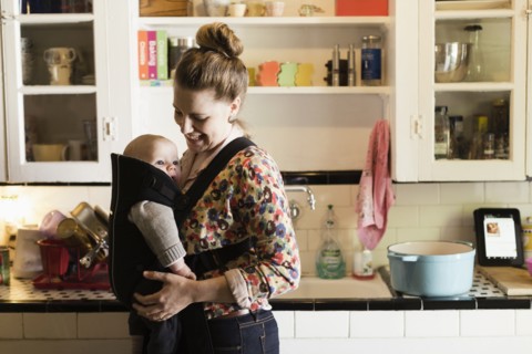 Mid adult mother with baby son in sling in kitchen