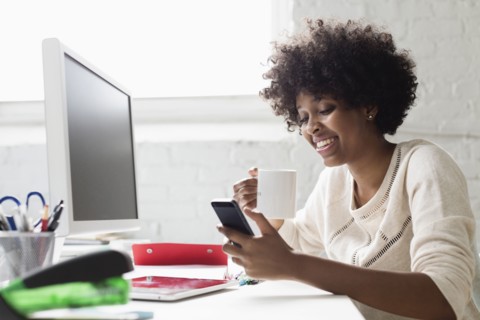 Young woman at desk with coffee using smartphone