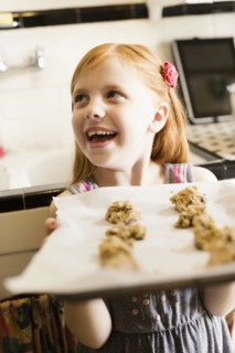 Girl holding up tray of biscuits in kitchen