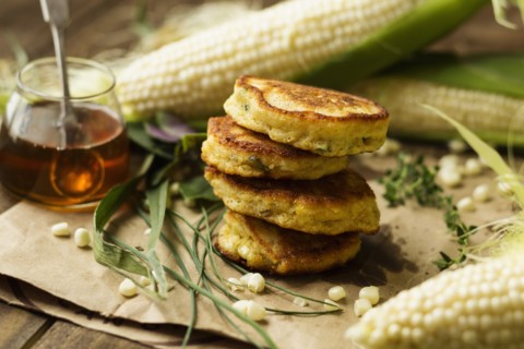 Stack of corn fritters with honey and corn cobs on kitchen table