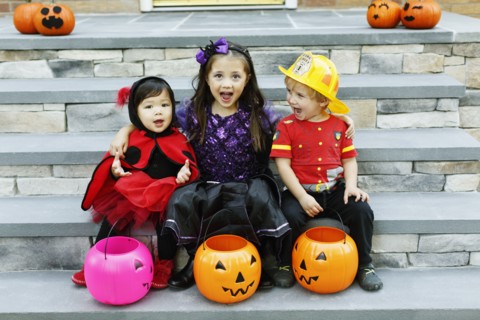 Three children sitting on steps with trick or treat buckets