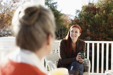 Senior woman and adult daughter chatting and drinking coffee on porch