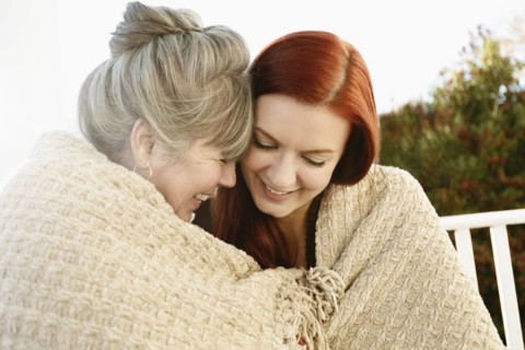 Senior woman and adult daughter face to face wrapped in a blanket on porch
