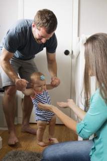 Mid adult man holding unsteady baby daughter hands whilst toddling in nursery