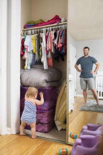 Mid adult man watching baby daughter search box in wardrobe