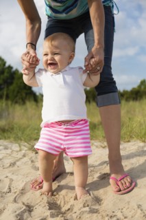 Mid adult woman holding baby daughters hands while toddling in sand