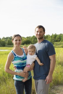 Portrait of mid adult parents carrying baby daughter by rural field
