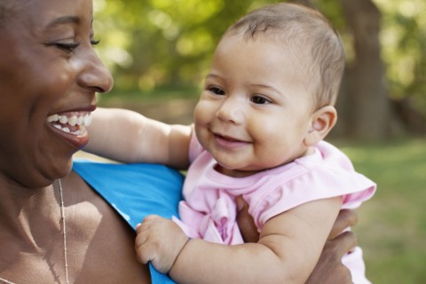 Head and shoulders of mother holding baby girl looking away smiling