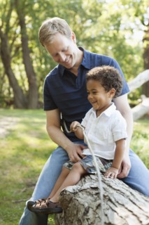 Father and son sitting on log holding twig smiling