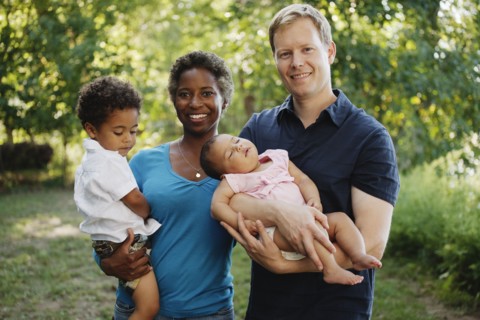 Family outdoors posing for photograph holding preschool boy and baby girl looking at camera smiling