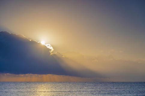 Sun rising behind clouds above sea