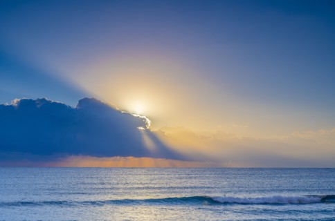 Sun rising behind clouds above sea