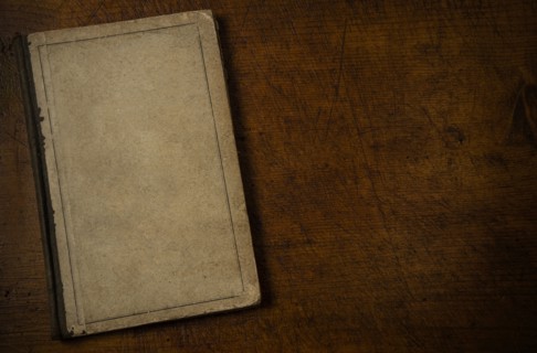 Old book with blank cover resting on old wooden desk top