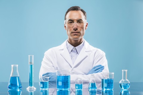 Portrait of scientist with beakers with blue liquid in foreground
