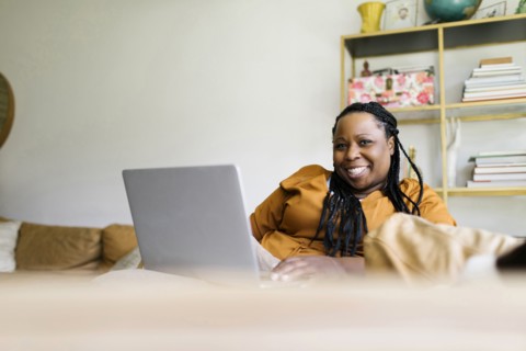 Smiling woman sitting on sofa and working on laptop