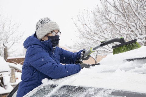 Woman in face mask removing snow from car