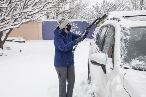 Woman in face mask removing snow from car
