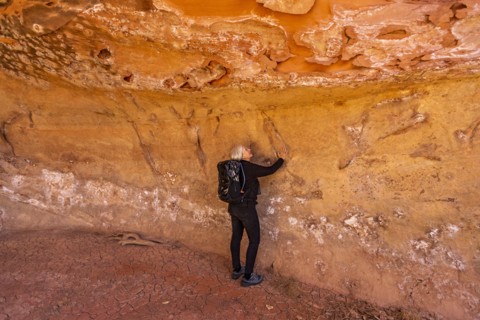 Woman touching sandstone cave wall in Grand Staircase-Escalante National Monument