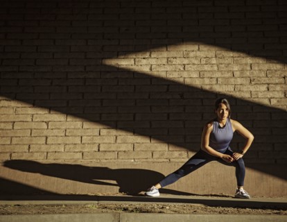 Woman stretching near brick wall in sunlight