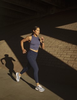 Woman jogging near brick wall in sunlight
