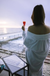 Rear view of woman with cocktail in hotel and observing sunrise over sea